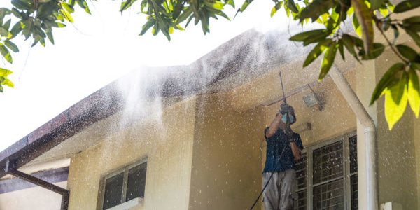 Worker using high pressure water jet spray gun to wash and clean dirt from roof ceiling at residential building